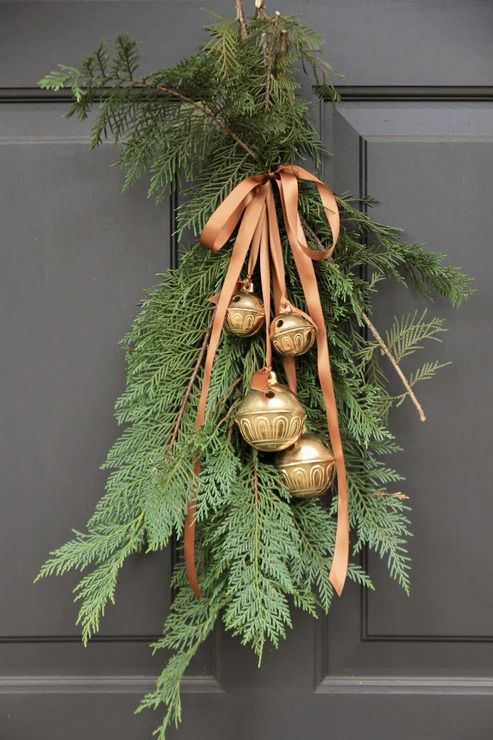 Sleigh Bells Elegant Christmas greenery with bronze ornaments and ribbon on a dark door for festive holiday decor. | Sky Rye Design Elegant Christmas greenery with bronze ornaments and ribbon on a dark door for festive holiday decor.