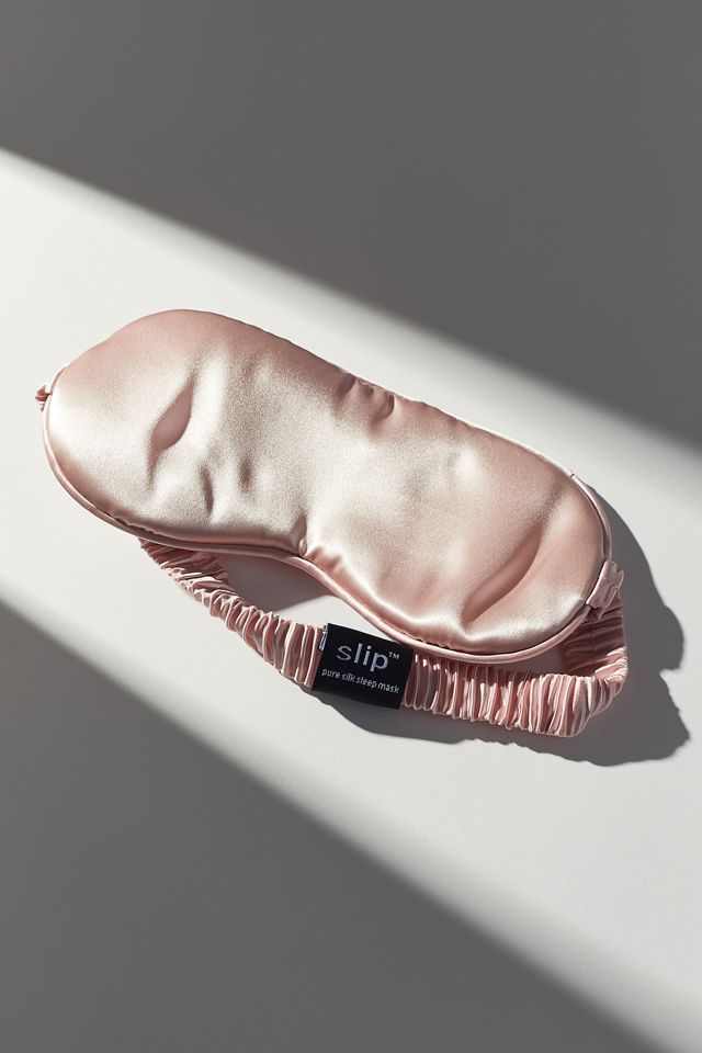 Pink silk sleep mask on a white surface with soft shadows, enhancing bedtime comfort and luxury style.