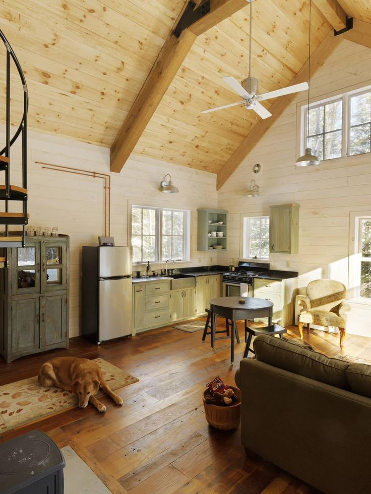 Small Home in Vermont Woods Cozy cabin interior with wooden beams, dog on rug, spiral staircase, and quaint kitchen. Warm, rustic decor. | Sky Rye Design Cozy cabin interior with wooden beams, dog on rug, spiral staircase, and quaint kitchen. Warm, rustic decor.