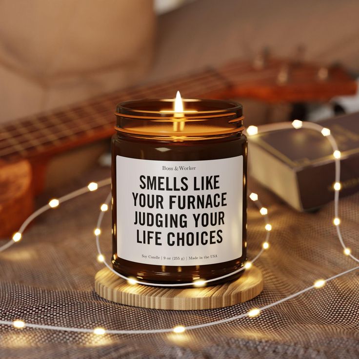 Smells Like Airflow Candle_ HVAC Technician Gift - Soy Wax Amber Jar Lit candle in cozy setting with humorous label, surrounded by string lights and guitar in background. | Sky Rye Design Lit candle in cozy setting with humorous label, surrounded by string lights and guitar in background.