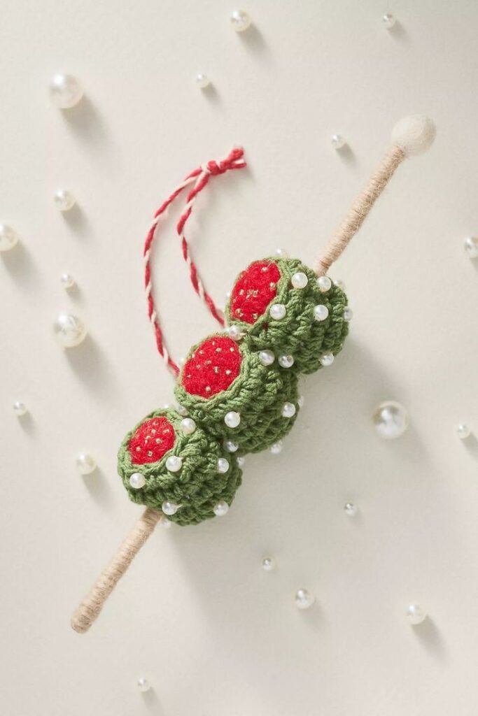 Snacks Sips Crochet Ornament Knitted green and red ornament with pearls and a twine loop, set against a pearl-studded background. | Sky Rye Design Knitted green and red ornament with pearls and a twine loop, set against a pearl-studded background.