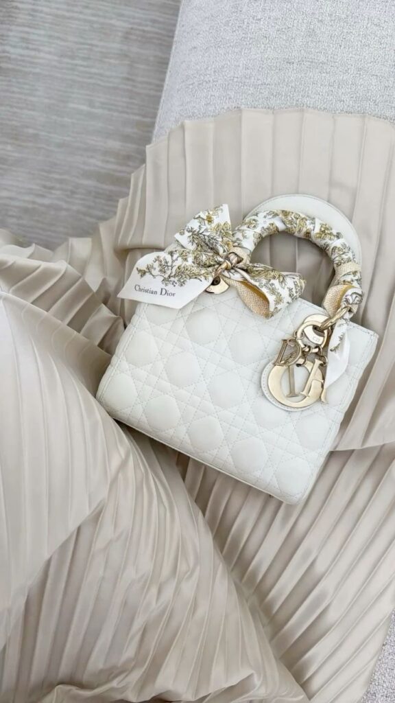 Soft Luxe🤍 Elegant white Christian Dior handbag with floral scarf on pleated fabric background. | Sky Rye Design Elegant white Christian Dior handbag with floral scarf on pleated fabric background.