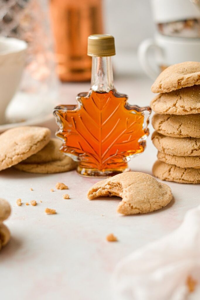 Soft Maple Cookies Maple syrup bottle with sugar cookies, one with a bite, on a light background. Perfect for autumn baking. | Sky Rye Design Maple syrup bottle with sugar cookies, one with a bite, on a light background. Perfect for autumn baking.