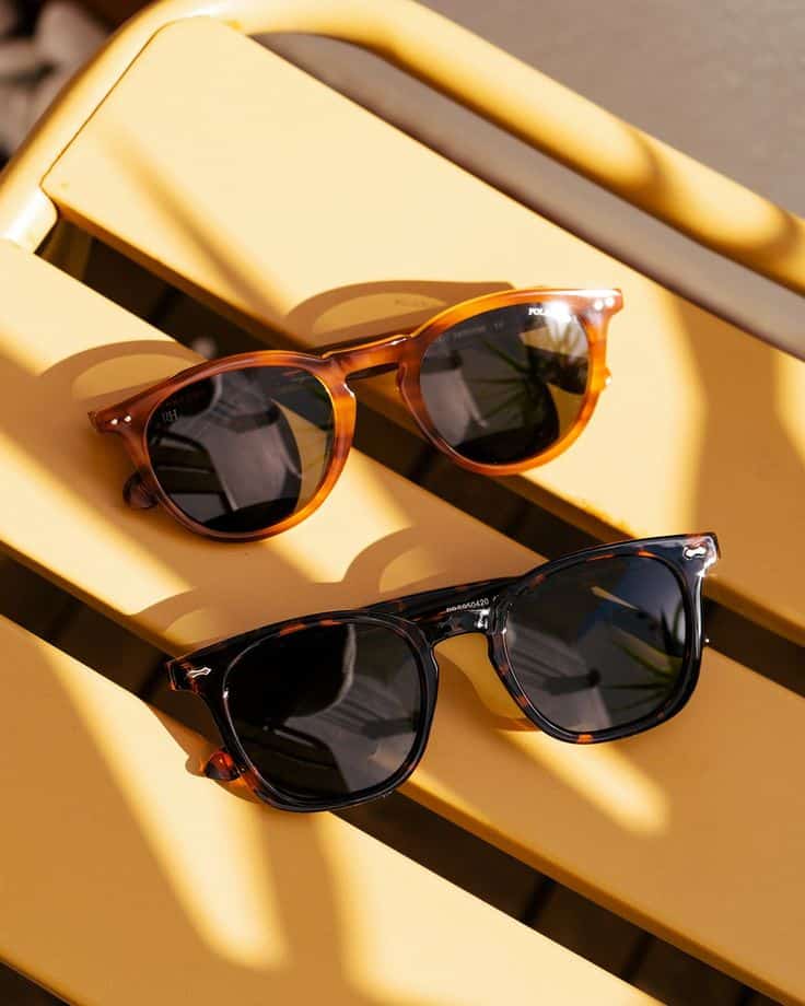 Sol e sombra no lugar certo a Opticalia Two stylish sunglasses with tortoiseshell frames on a yellow chair, casting shadows in the sunlight. | Sky Rye Design Two stylish sunglasses with tortoiseshell frames on a yellow chair, casting shadows in the sunlight.