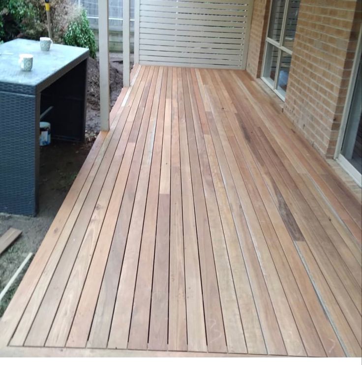 Spotted Gum Decking Newly built wooden deck with modern outdoor table on a residential patio next to a brick wall. | Sky Rye Design Newly built wooden deck with modern outdoor table on a residential patio next to a brick wall.