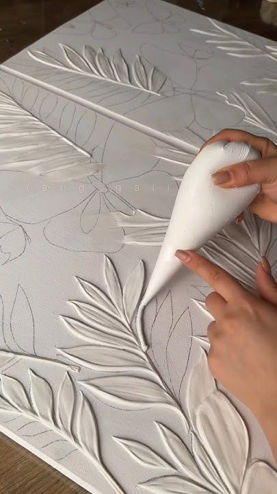 Artist creating textured leaf pattern on canvas with white paste for decorative art piece.