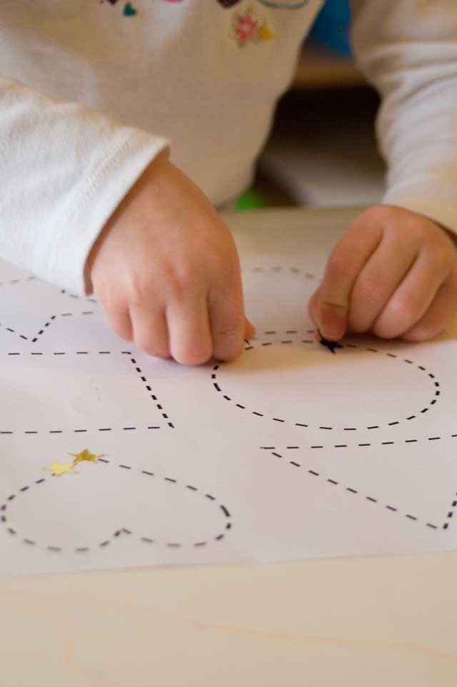 Sticker Shapes Child's hands tracing dotted heart lines on paper for a fun and educational activity. | Sky Rye Design Child's hands tracing dotted heart lines on paper for a fun and educational activity.