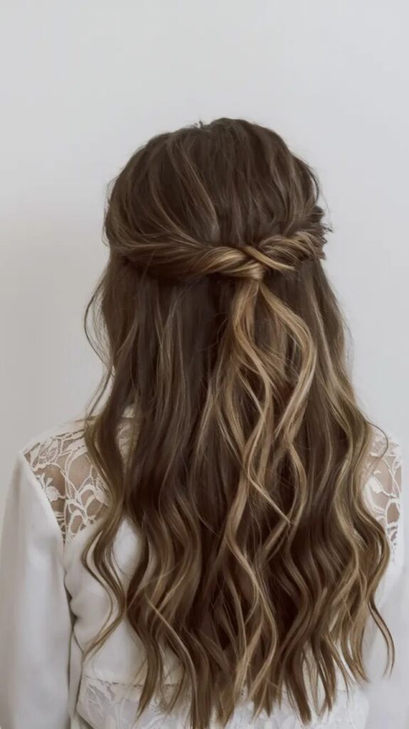 Woman with long, wavy brown hair styled in a half-up braid, wearing a lace white top. Elegant hairstyle rear view.