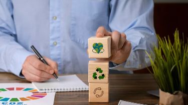 Person stacking eco-themed blocks at desk, symbolizing sustainability with recycling icons and a notebook.