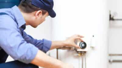 Plumber adjusting water heater thermostat in uniform for residential maintenance service.