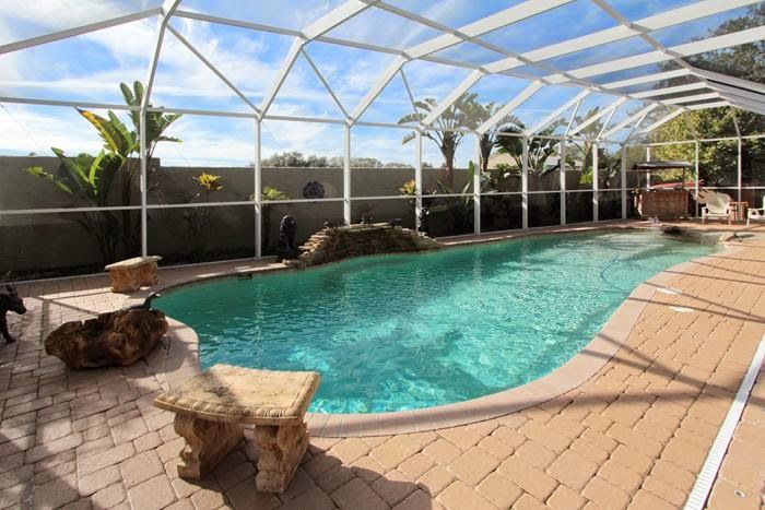 Tampa Real Estate News Enclosed backyard pool with stone tiles and tropical plants under a clear blue sky. | Sky Rye Design Enclosed backyard pool with stone tiles and tropical plants under a clear blue sky.
