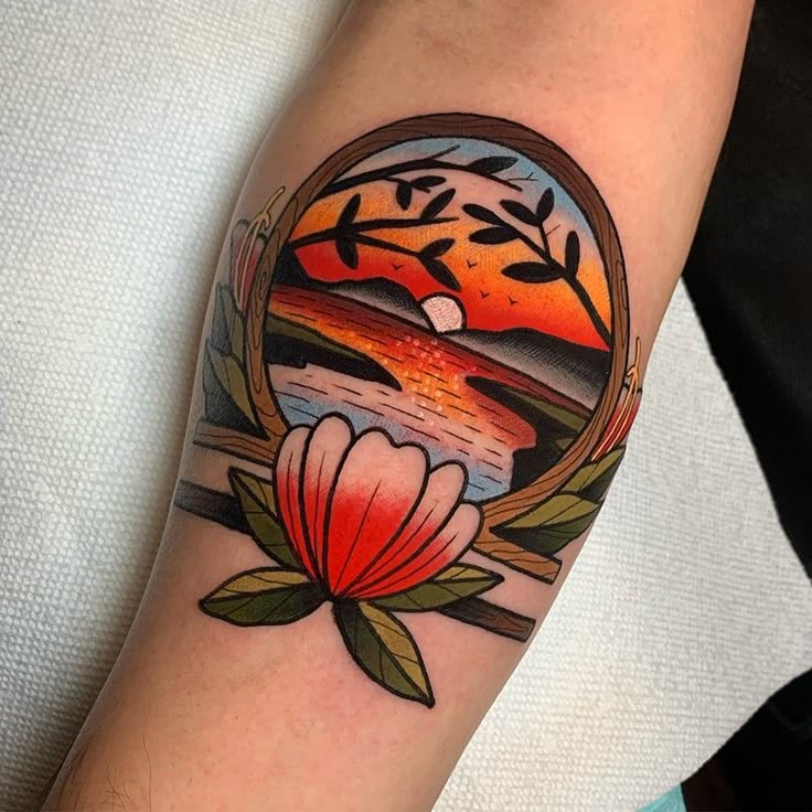 Colorful tattoo of a sunset with ocean waves framed by a flower, featuring vibrant reds, oranges, and greens.