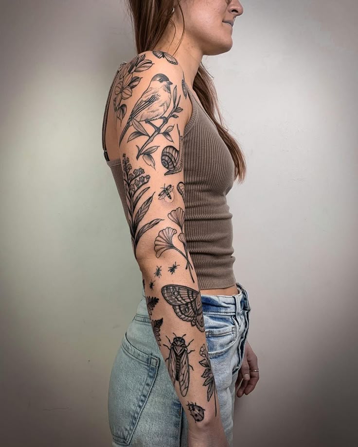 Person with detailed black ink nature-themed sleeve tattoo on arm, featuring birds, insects, and leaves.