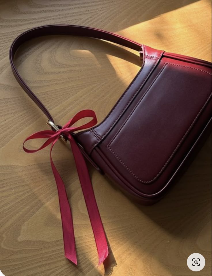 The Monthly Edit_ december MMXXIII Era Design House Elegant maroon handbag with a decorative bow, laying on a wooden surface in soft lighting. | Sky Rye Design Elegant maroon handbag with a decorative bow, laying on a wooden surface in soft lighting.