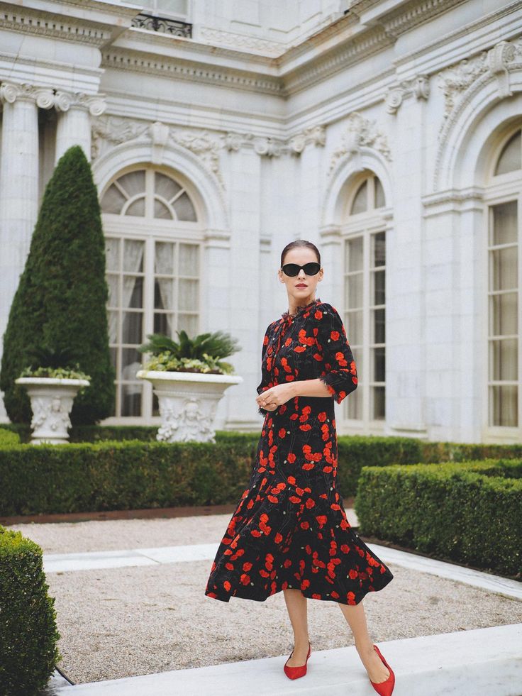 The Season Of Dark Florals - BITTERSWEET COLOURS Woman in floral dress and sunglasses walks in front of elegant building with arched windows and greenery. | Sky Rye Design Woman in floral dress and sunglasses walks in front of elegant building with arched windows and greenery.