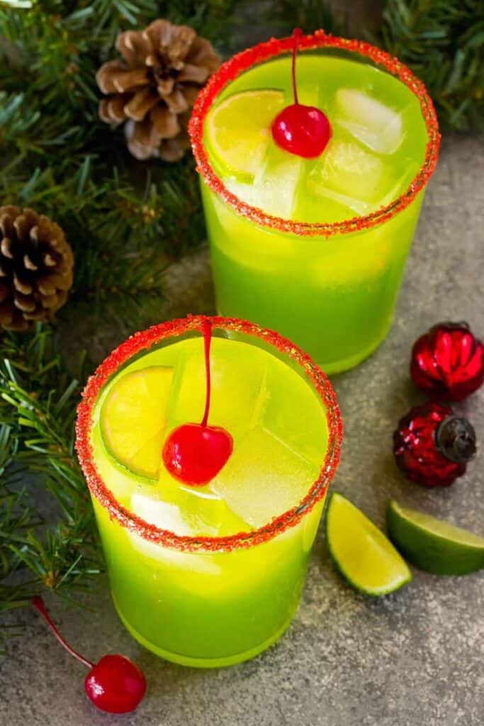 Festive green cocktails with lime slices, cherries, and red-rimmed glasses, surrounded by holiday decorations.