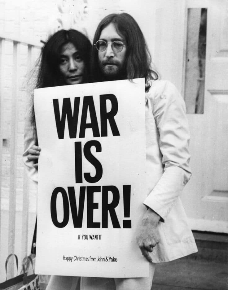 Two people holding a War Is Over poster, advocating for peace and celebrating Christmas.