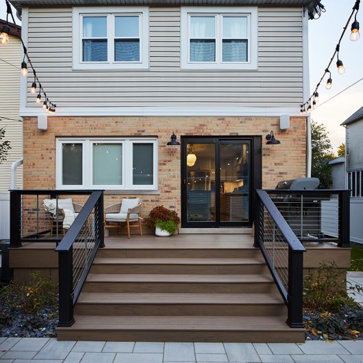 Modern back patio with string lights, cozy seating, and steps leading to sliding doors on a brick and siding house.
