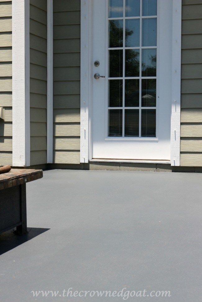 White-framed glass door opening to a sunny patio with smooth gray flooring and light green siding.