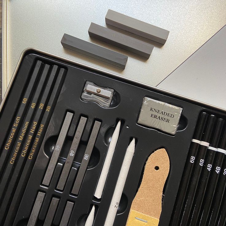 Art supplies set with charcoal sticks, pencils, kneaded eraser, and sharpener organized in a box.
