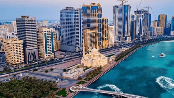 Top Reasons to Invest in Sharjah Real Estate in Aerial view of Sharjah city skyline with mosque and waterfront, showcasing modern skyscrapers and vibrant blue water. | Sky Rye Design Aerial view of Sharjah city skyline with mosque and waterfront, showcasing modern skyscrapers and vibrant blue water.