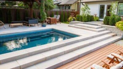 Modern backyard swimming pool with surrounding patio seating area, wooden deck, and lush garden landscaping.