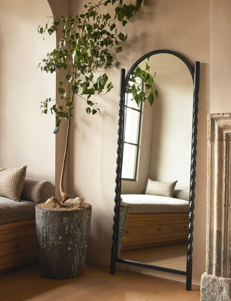 Elegant interior with tall floor mirror, green potted plant, cushioned bench, and window, creating a cozy, serene space.