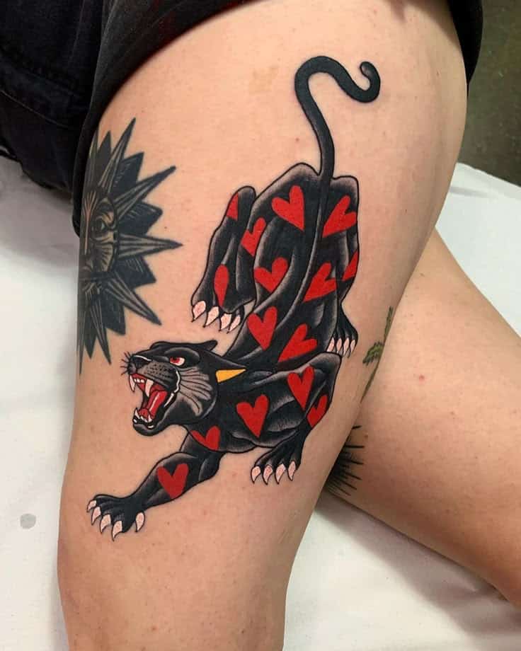 Panther tattoo with red hearts on thigh, featuring bold colors and traditional style design.