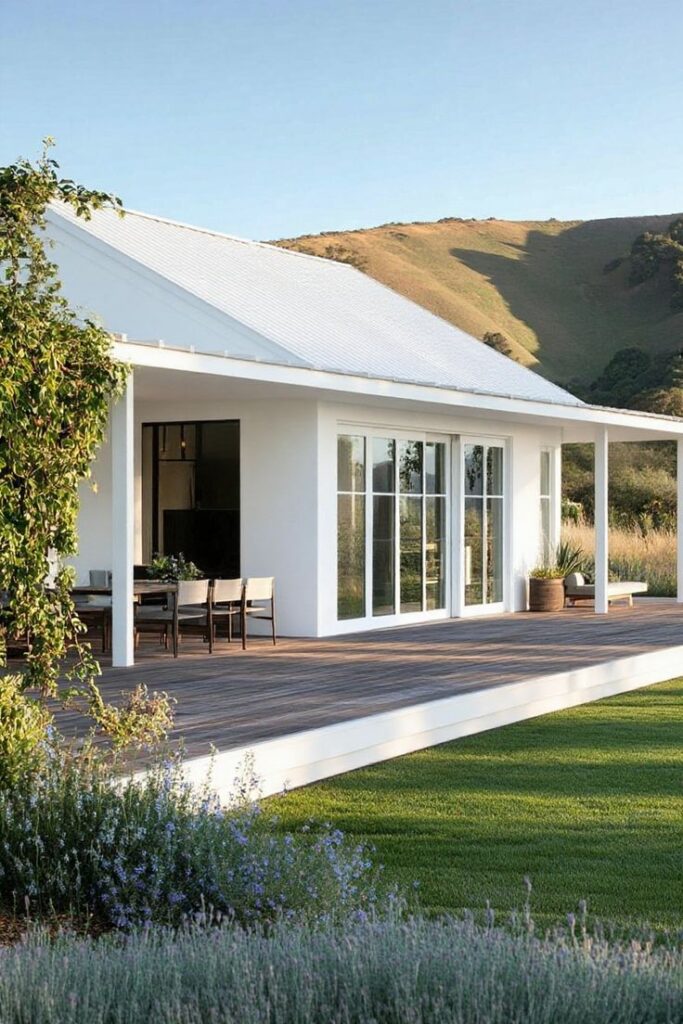 Transcendent Terrace Retreat_ Vine-Covered Elegance_ Long House Floor Plans Modern white house with large deck, surrounded by greenery and mountains in the background. | Sky Rye Design Modern white house with large deck, surrounded by greenery and mountains in the background.