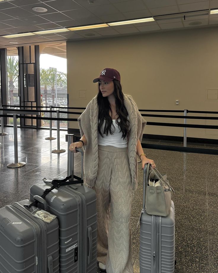 Woman in airport with luggage, wearing a hat and cozy outfit, ready for travel.