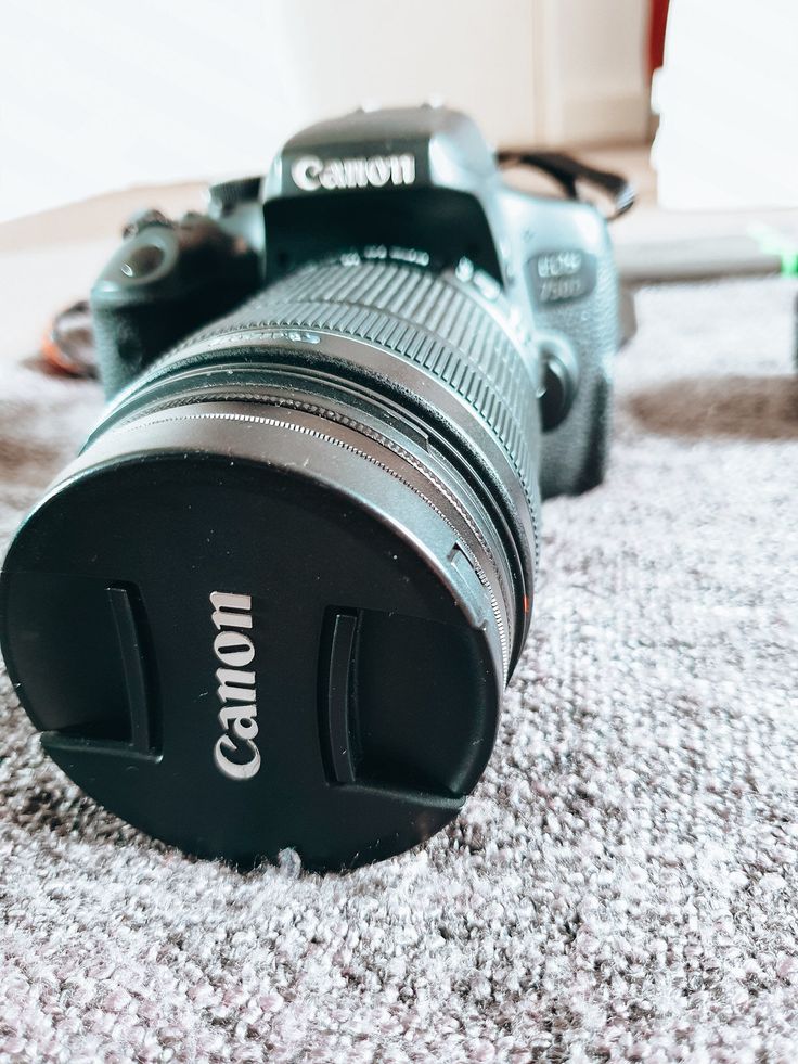 Close-up of a Canon DSLR camera lens on a textured surface, highlighting brand and lens details.
