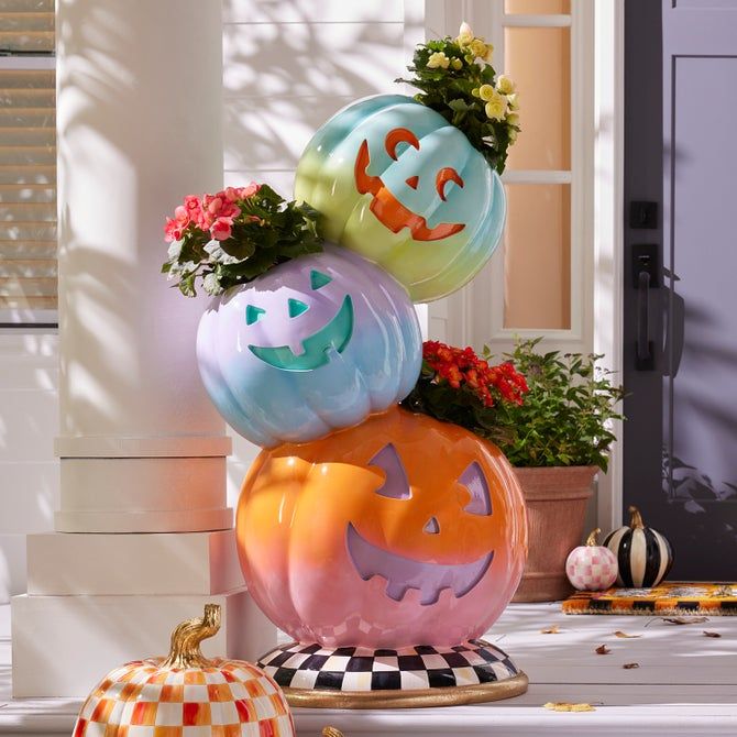 Colorful Halloween pumpkin stack with flowers on porch, festive autumn decor.