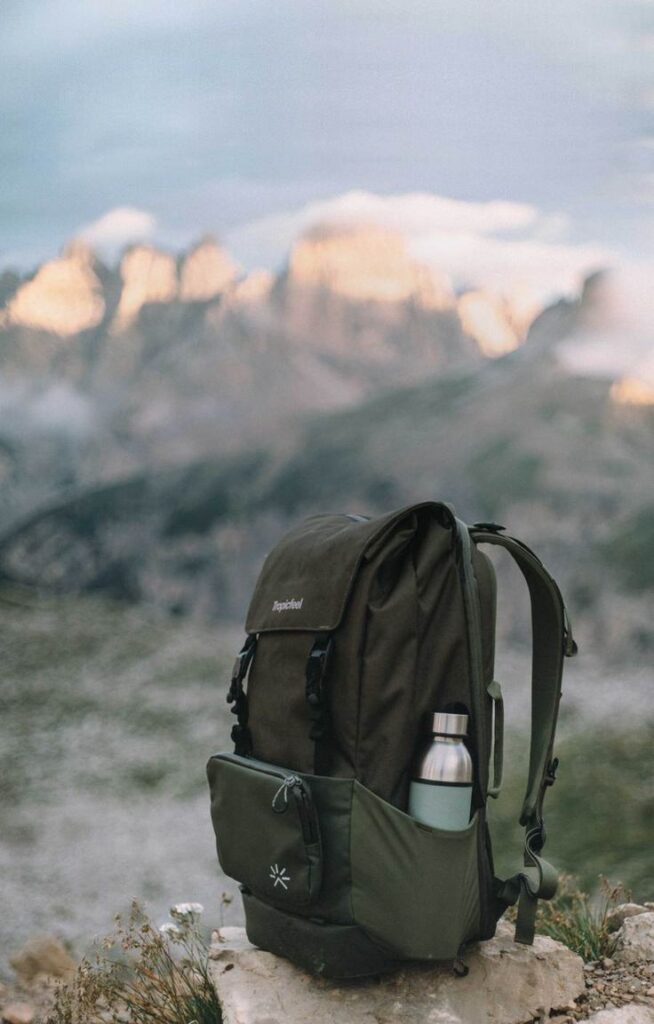 Green hiking backpack with a water bottle, set against a mountain landscape background. Perfect for outdoor adventures.