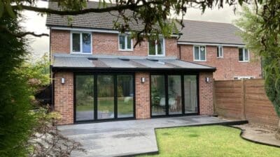 Modern brick house with large glass patio doors, gray roof, and a lush green garden.