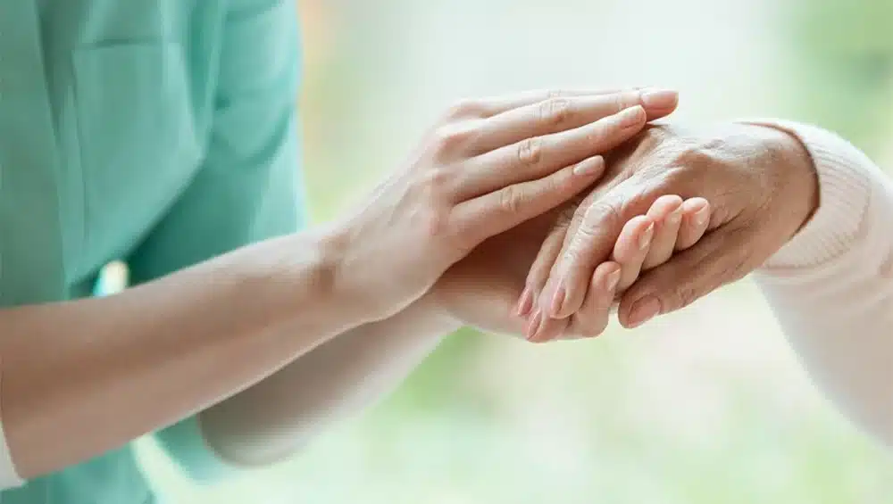 Caregiver gently holding elderly person's hand, symbolizing compassion and support in aged care.