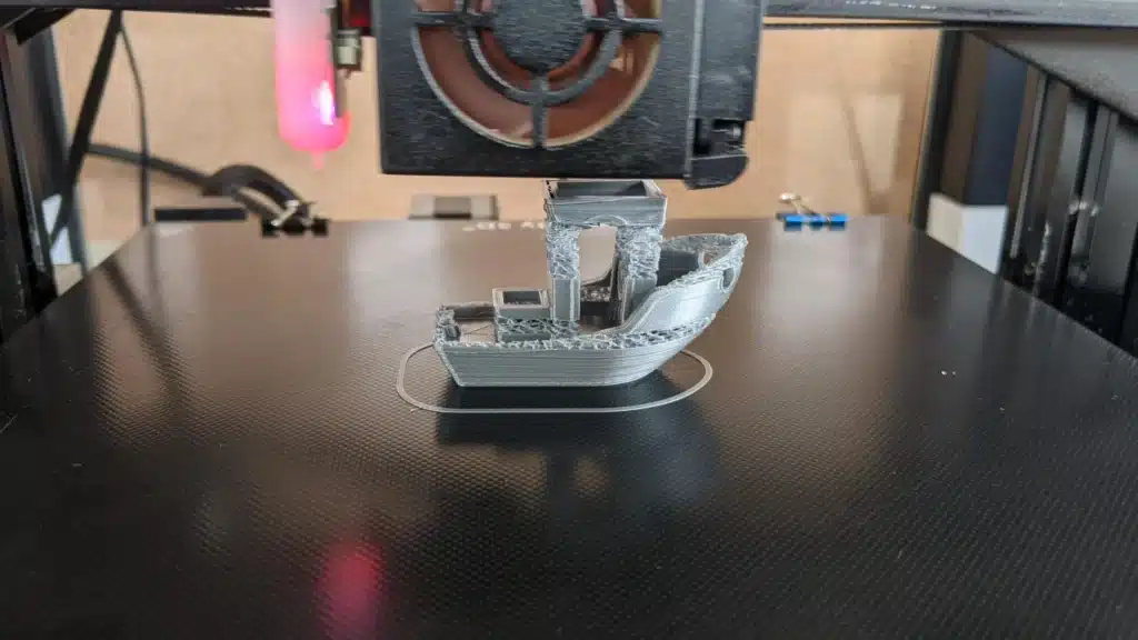 Under-extrusion-lead-scaled 3D printer creating a partially completed small boat model on a black surface. | Sky Rye Design 3D printer creating a partially completed small boat model on a black surface.