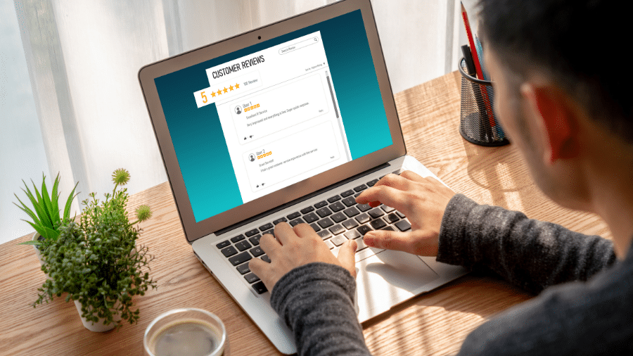 Untitled Design - 1 Person reading customer reviews on a laptop, star rating visible, sunny desk setup with a plant and coffee. | Sky Rye Design Person reading customer reviews on a laptop, star rating visible, sunny desk setup with a plant and coffee.