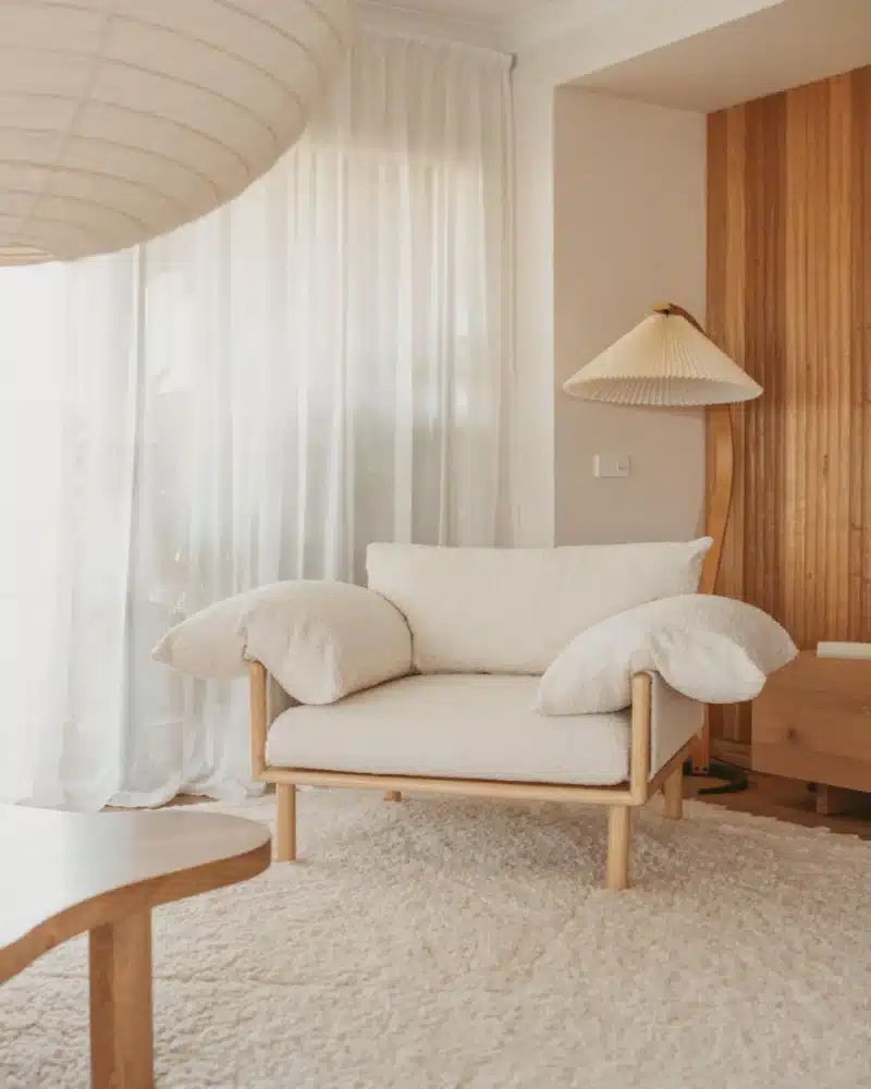 | Sky Rye Design Cozy modern living room with a plush white armchair, wooden lamp, and soft textured rug.