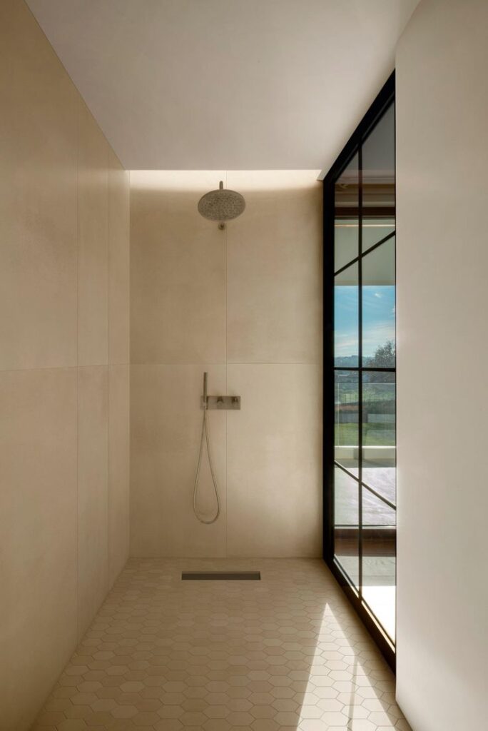 Minimalist shower design with beige tiles and glass wall, offering a bright and open bathroom space.