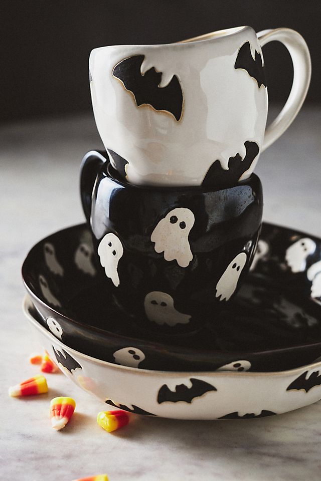 Halloween-themed cups and plates with ghost and bat designs, surrounded by candy corn on a marble surface.