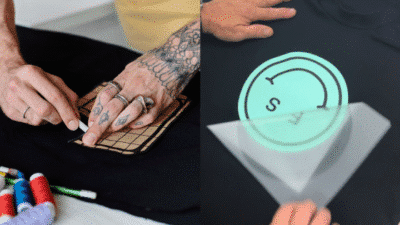 Tattooed hands applying custom designs on black t-shirts.