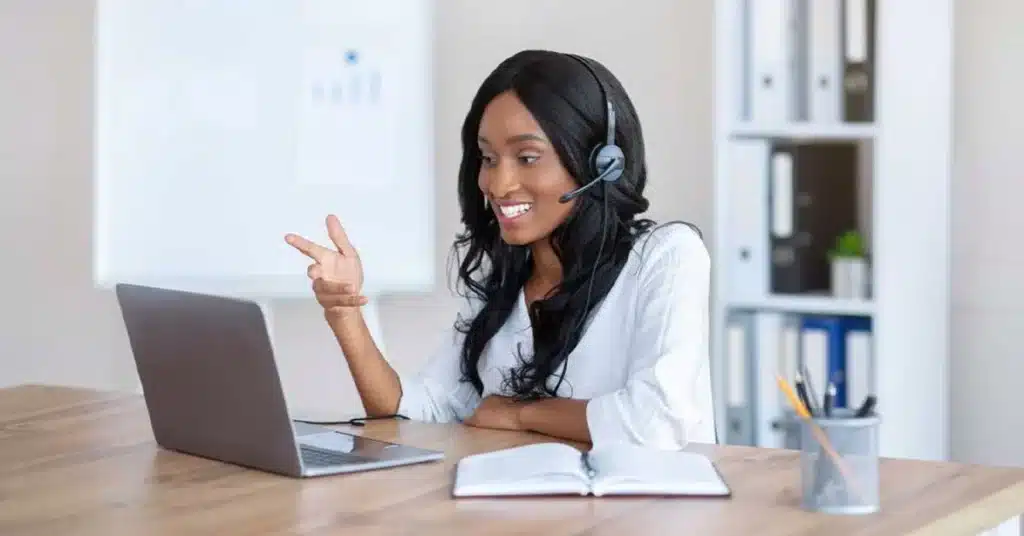 Virtual-Medical-Assistant- Smiling woman on a video call wearing a headset, using a laptop in a modern office setting. | Sky Rye Design Smiling woman on a video call wearing a headset, using a laptop in a modern office setting.