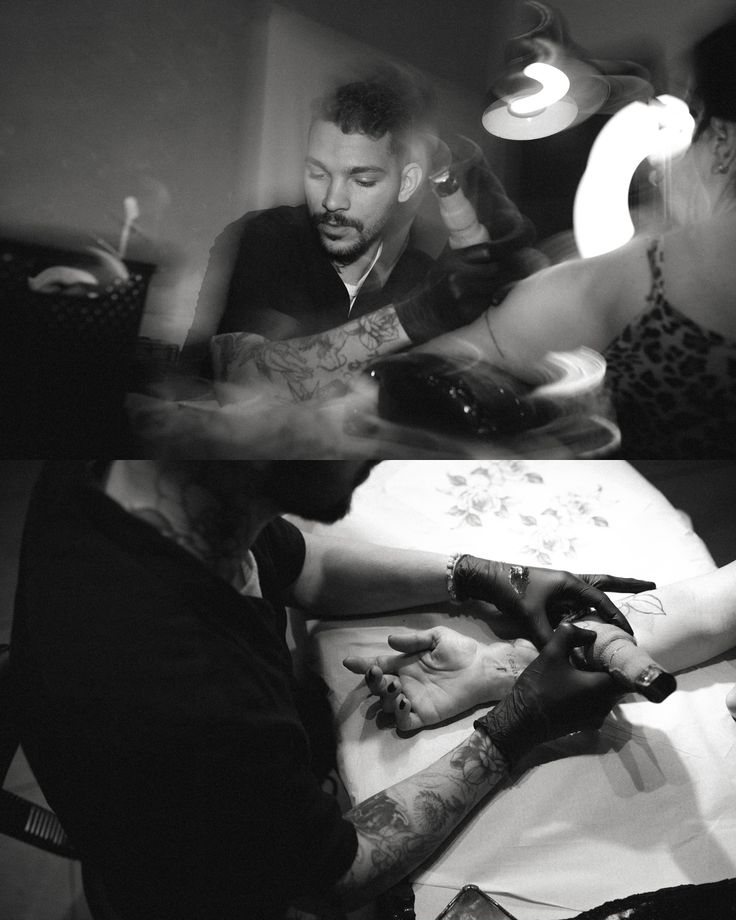 Tattoo artist focuses on intricate arm design in a dimly lit studio, highlighting creative process in black and white.