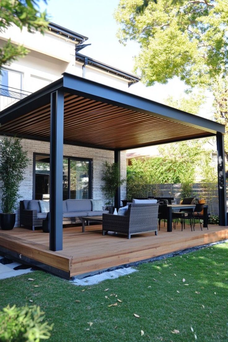 Modern outdoor patio with pergola, wicker furniture, and dining area on wooden deck amidst lush greenery.