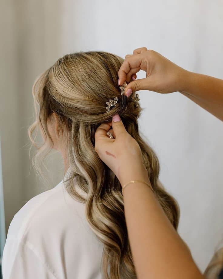 Stylist pinning elegant bridal hairstyle with decorative clip on wavy blonde hair.