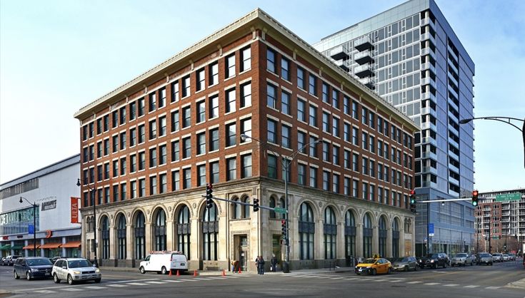 Historic brick building on a busy city street corner, contrasting with a modern glass high-rise behind it.