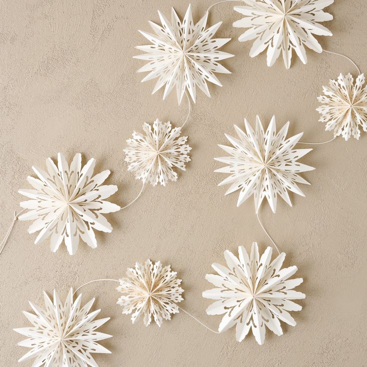 Whimsical Snowflake Garland Paper star decorations on beige background, creating a festive and elegant holiday atmosphere. | Sky Rye Design Paper star decorations on beige background, creating a festive and elegant holiday atmosphere.