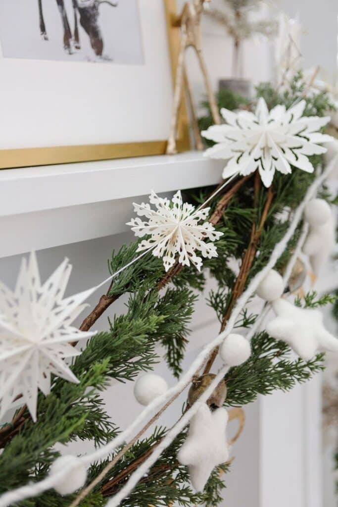 White Paper Snowflake Garland Festive fireplace decor with white paper snowflakes and green garland, creating a cozy holiday atmosphere. | Sky Rye Design Festive fireplace decor with white paper snowflakes and green garland, creating a cozy holiday atmosphere.