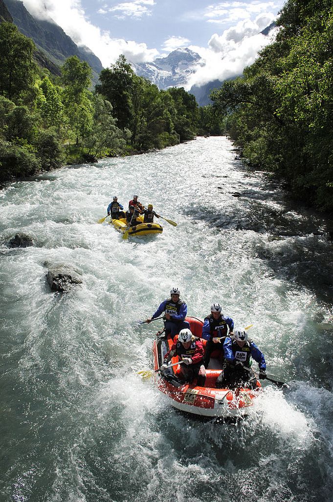 Group enjoying white water rafting adventure on a scenic, lush mountain river under a blue sky.