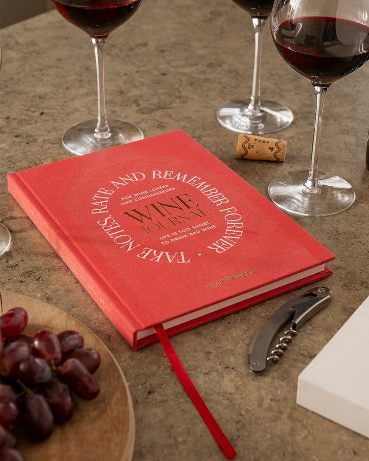 Wine Tasting Red wine journal with open corkscrew on table, surrounded by wine glasses and grapes for wine tasting notes. | Sky Rye Design Red wine journal with open corkscrew on table, surrounded by wine glasses and grapes for wine tasting notes.